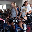 Students cycling on stationary bikes and smiling in an indoor studio