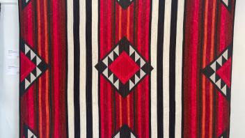 large quilt with geometric patterns of lines and triangles in red black and white