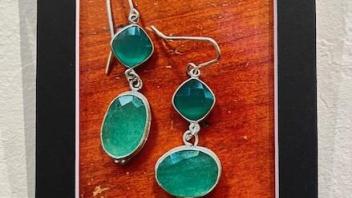 Silver earrings with green stones displayed in a black frame against a wooden background.
