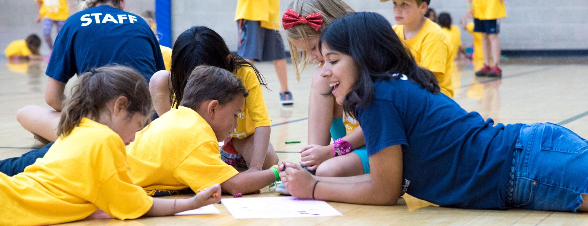 Camp counselor sitting with kids and drawing on the floor of a gym