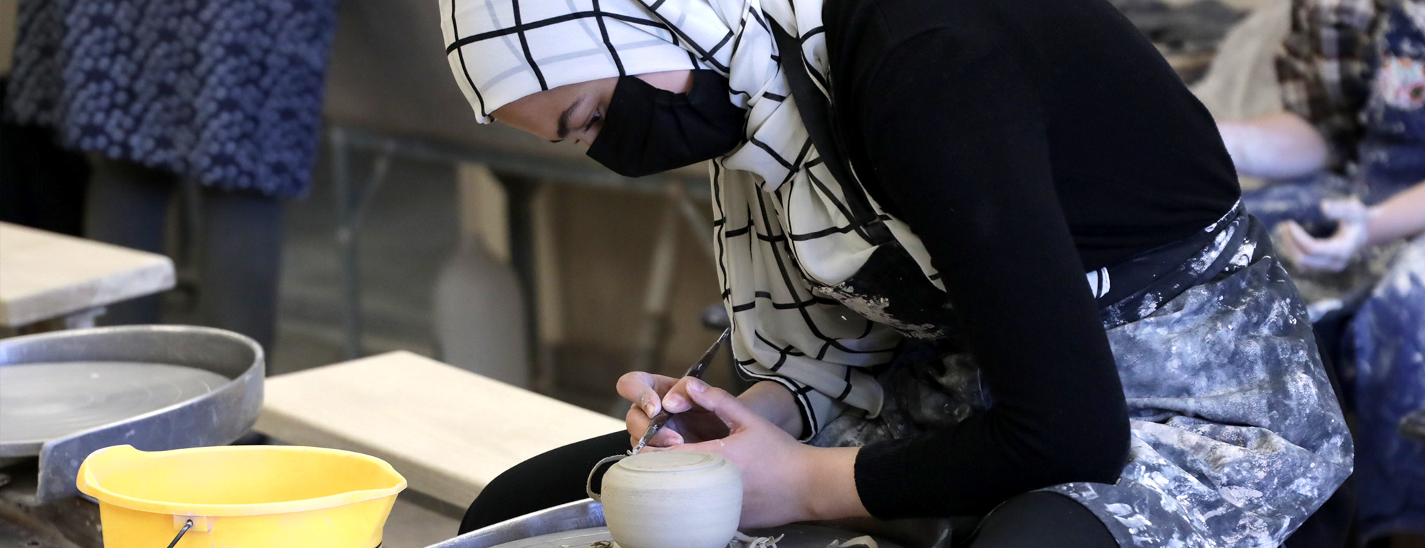 UC Davis student uses a tool to shape clay on a pottery wheel