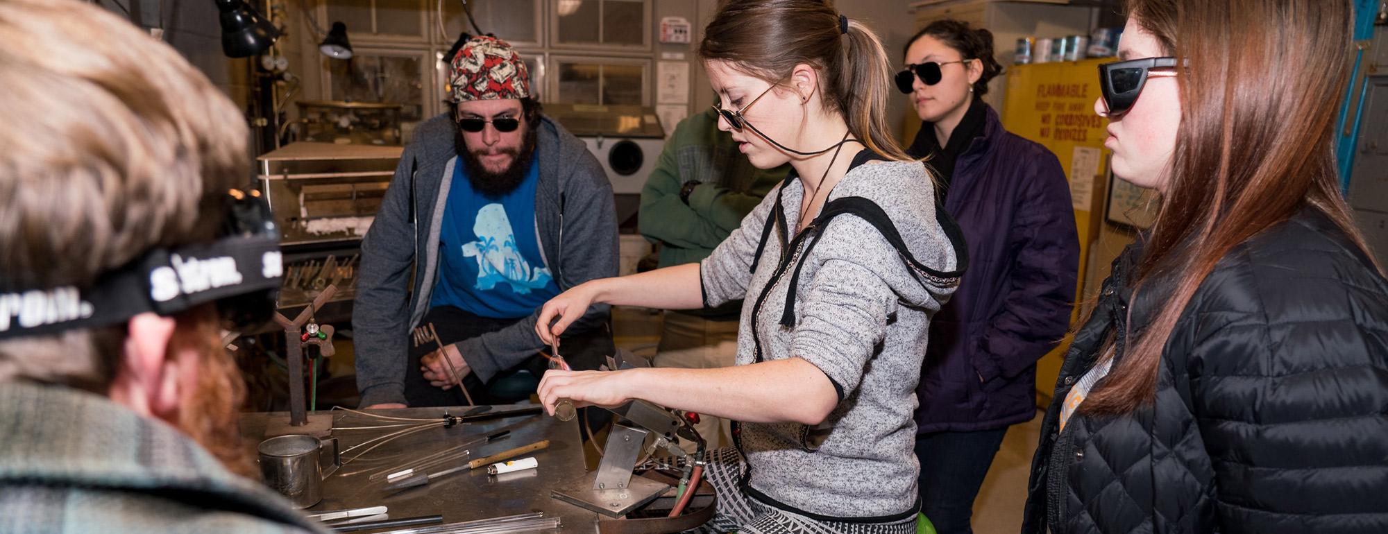 A student works with glass and a flamethrower while others look on