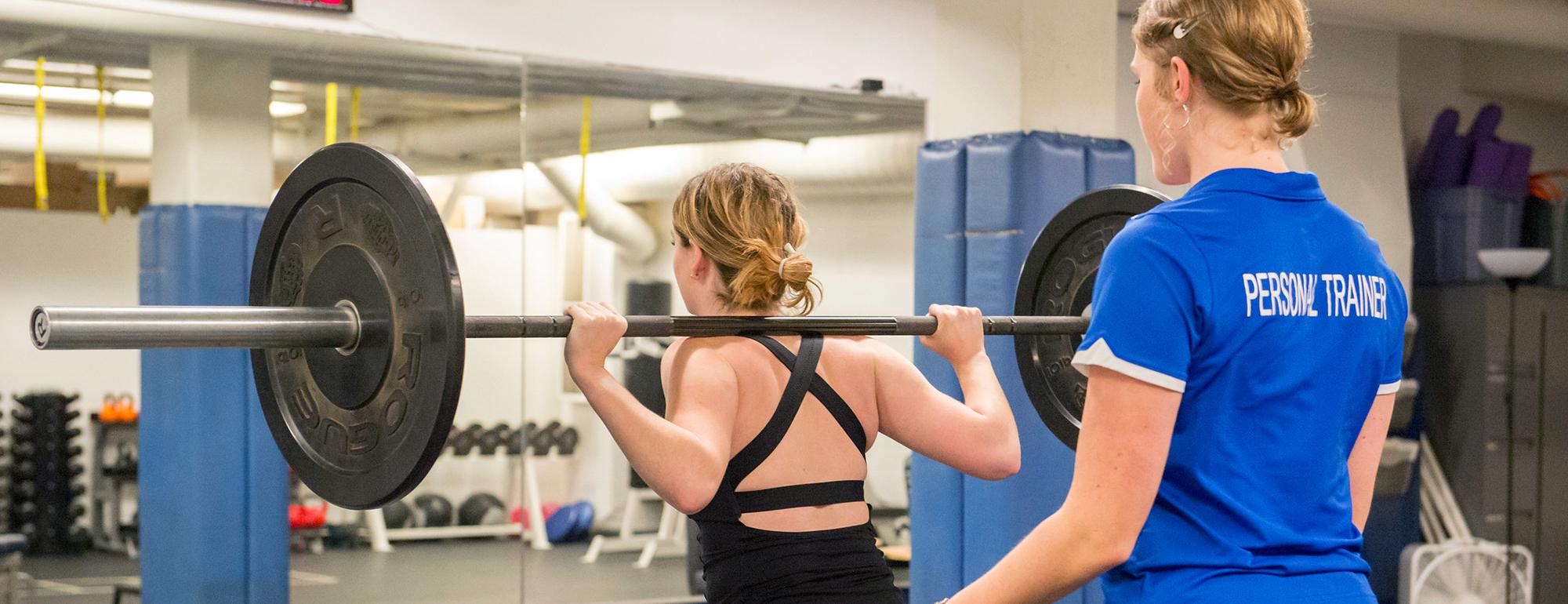 Personal trainer stands behind woman lifting weights