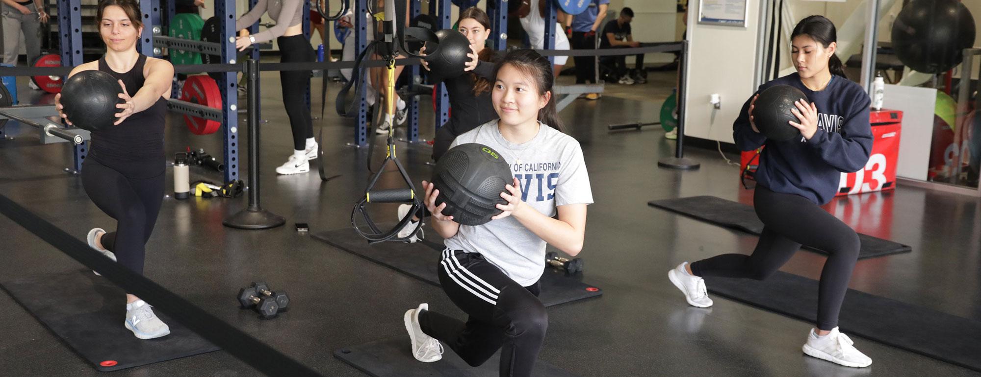 Students perform lunge exercise while holding medicine balls