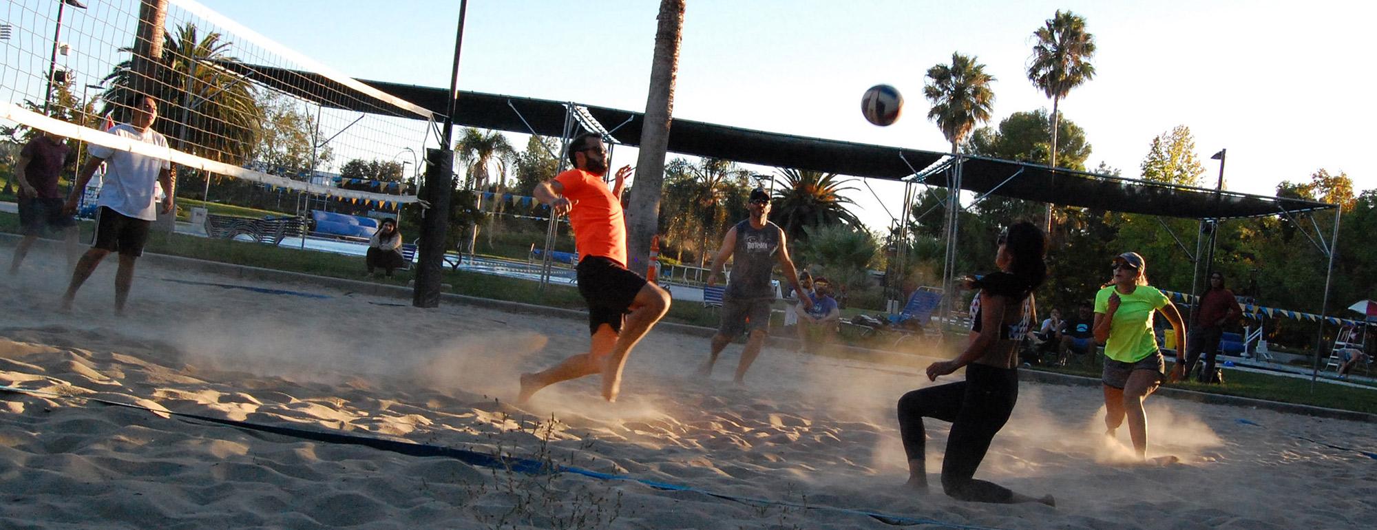 Students playing volleyball on an outdoor sand court at sunset
