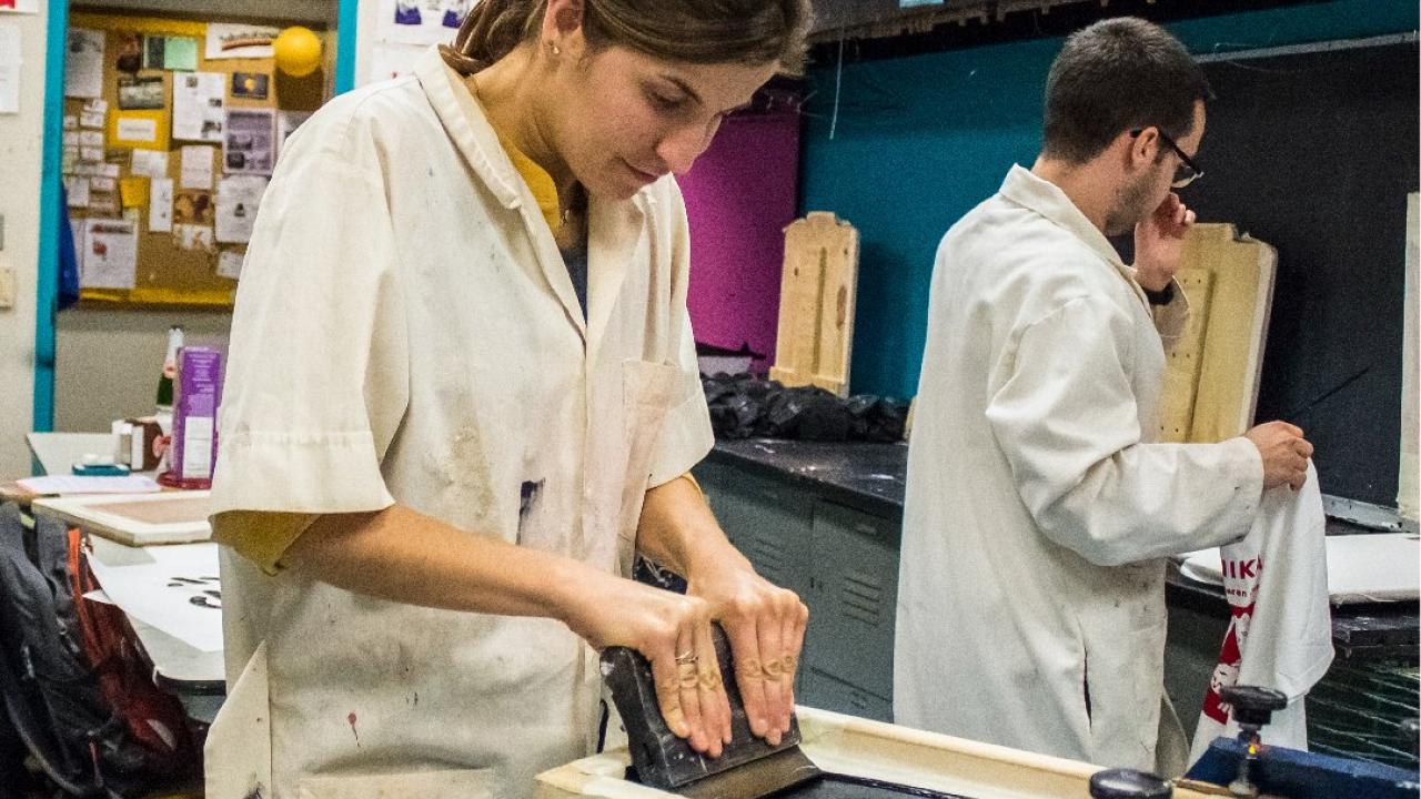 a female student screenprinting shirt by pressing ink into silk screen mesh