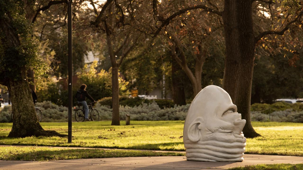 The "eye on Mrak" egghead sits in the righthand side of the frame. Two bikers cycle passed in the background.