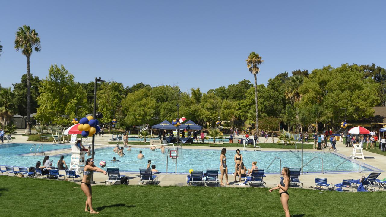 two students play volleyball with the rec pool facility in the background