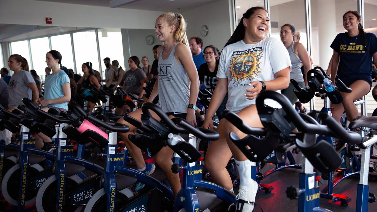 Students cycling on stationary bikes and smiling in an indoor studio