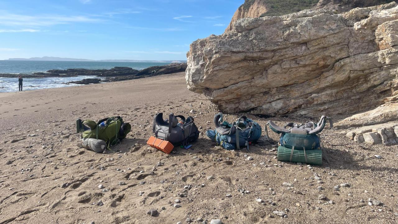 4 backpacks laying in the sand with the ocean in the background