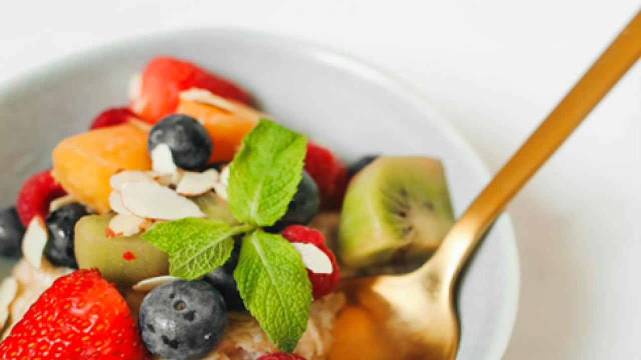 A bowl of oatmeal with fruit and a spoon.
