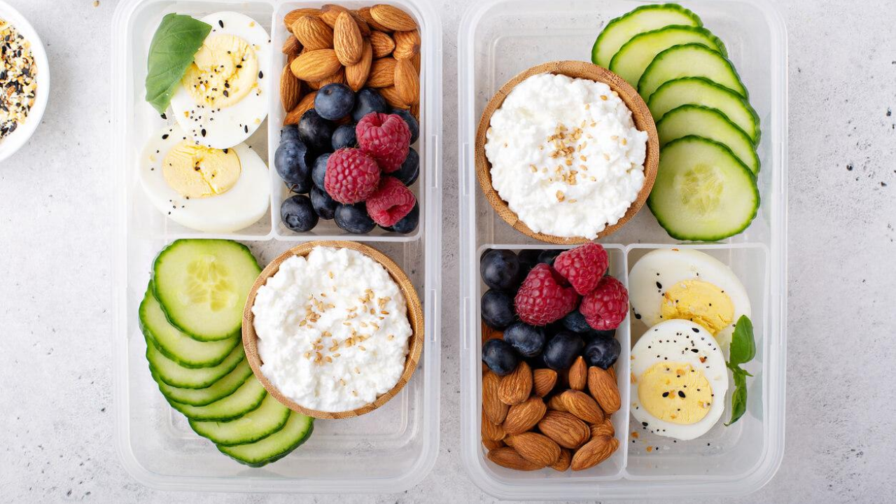 Two identical plastic tupperware with cucumbers and cottage cheese, almonds and berries, and hard boiled eggs in individual compartments.