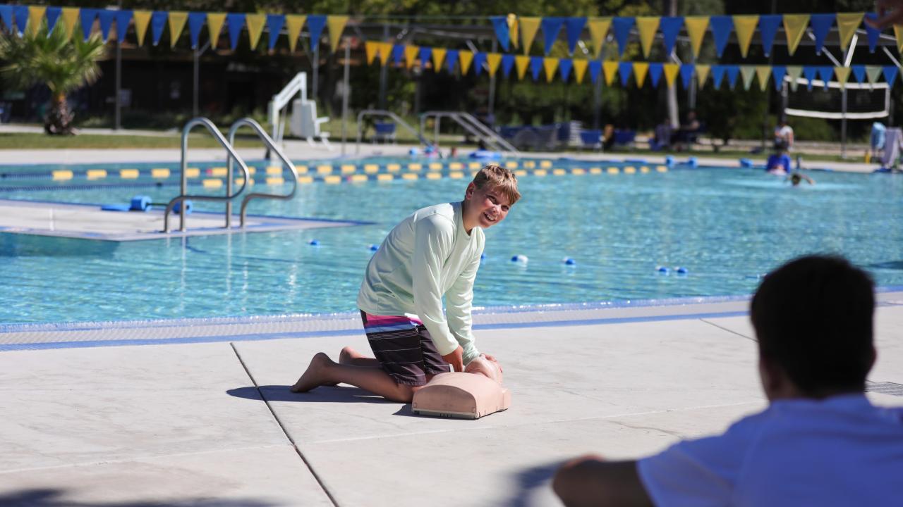 a camper practices CPR on a dummy by the Rec Pool.