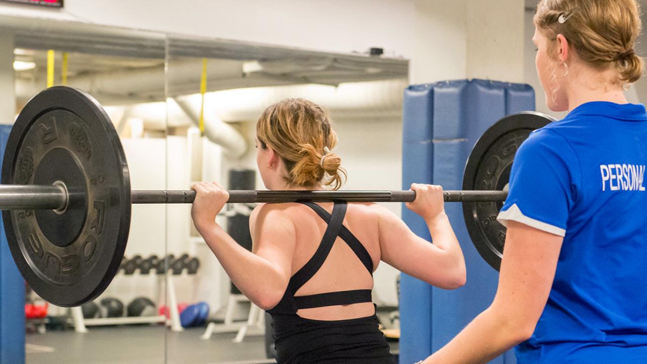 Personal trainer stands behind woman lifting weights