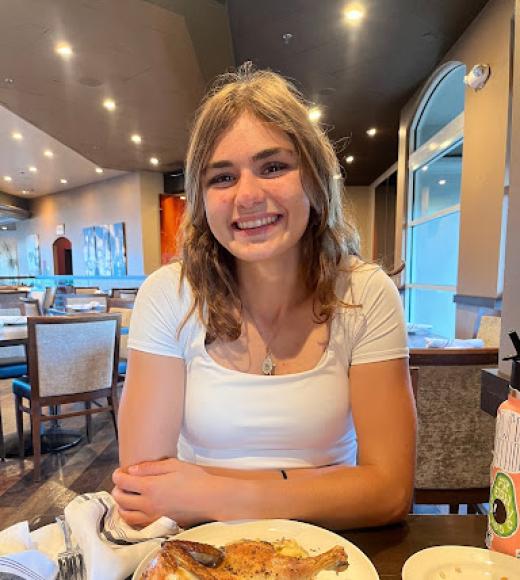 Audrey sits at a table in front of a plate of food and smiles for the camera.
