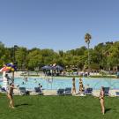 two students play volleyball with the rec pool facility in the background