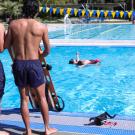 Two male student staff members are facing the pool, observing an individual in the pool as part of lifeguard training.