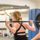 Personal trainer stands behind woman lifting weights