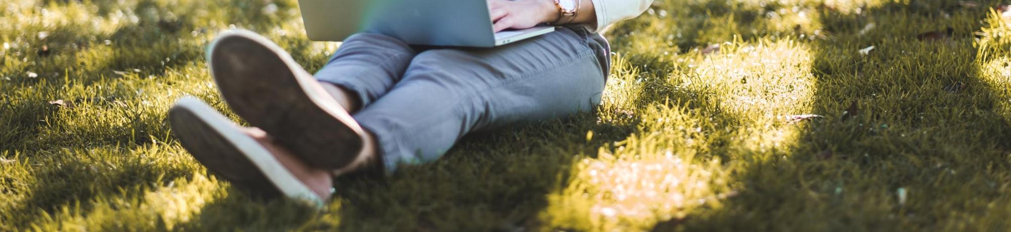 Girl on laptop sitting outdoors under tree