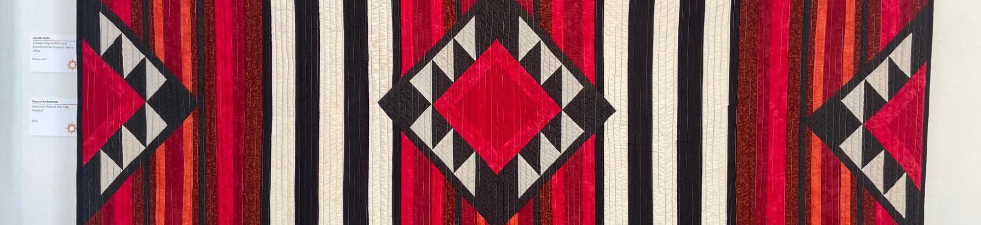 large quilt with geometric patterns of lines and triangles in red black and white