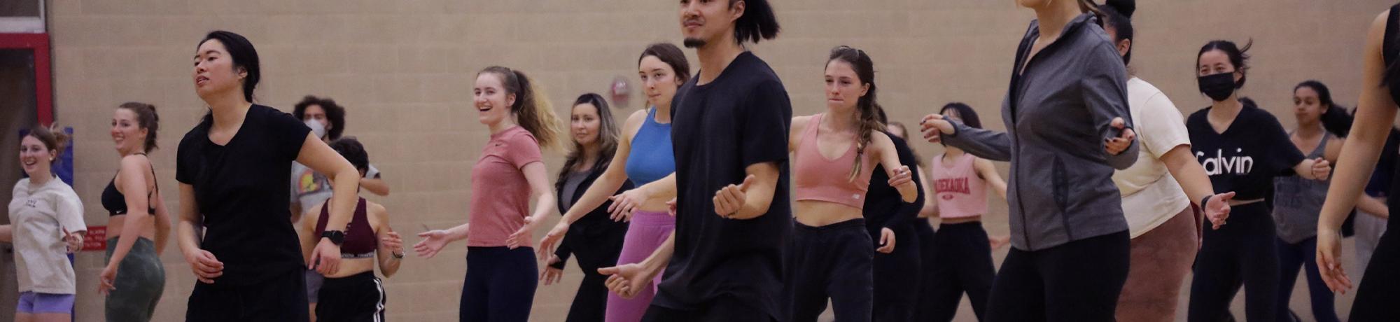 A large group of students does Zumba in an indoor gym
